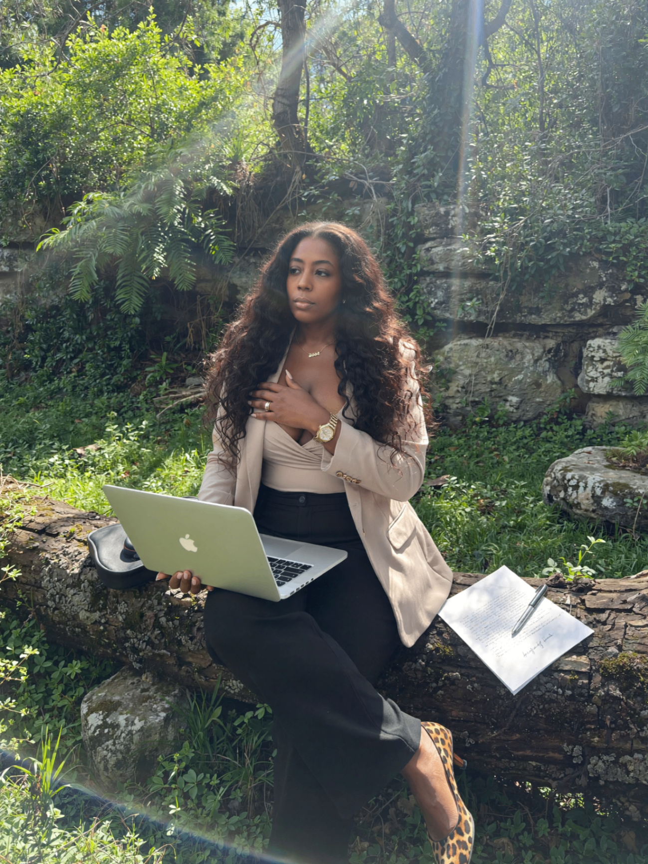 Tarean working from a moss-covered ledge in the woods, laptop open, leopard heels on